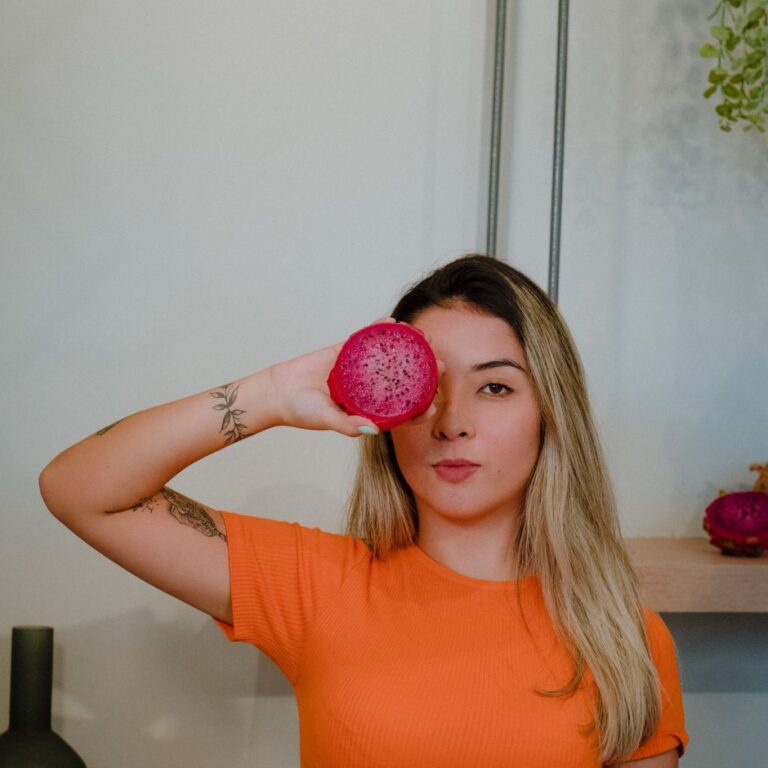 Julia Jiang, nutricionista, segurando metade de uma pitaya vermelha na frente de um dos olhos